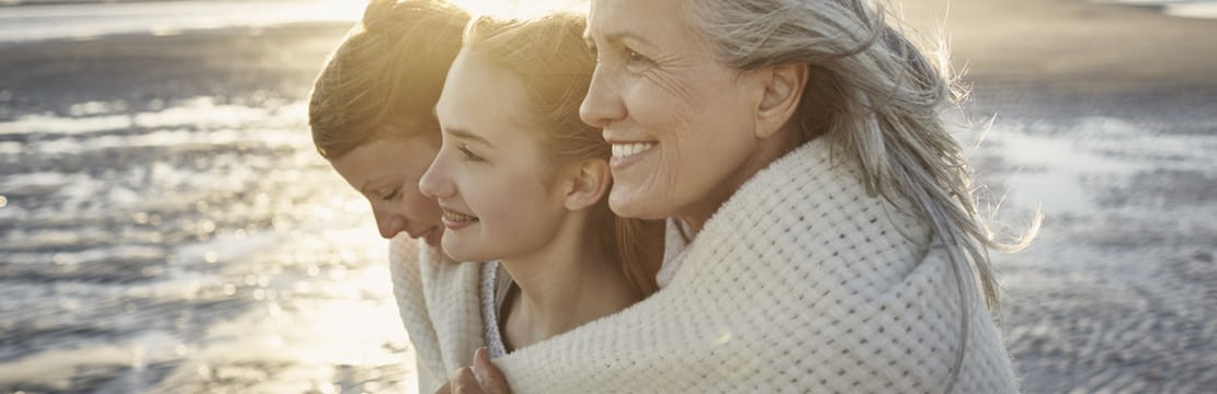 Grandmother, mother and daughter wrapped in a blanket on the beach